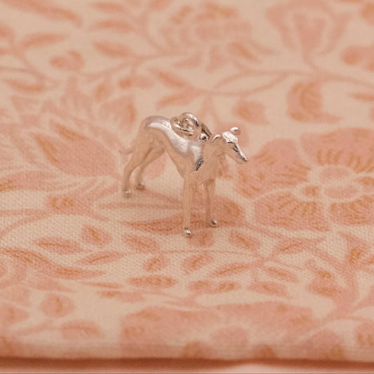 Small silver whippet dog figurine on a pink floral fabric background